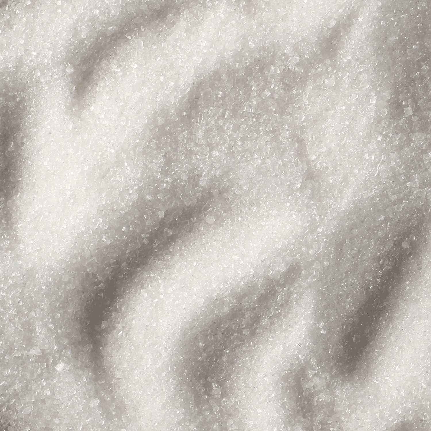 Close-up view of white granulated sugar, mirroring the crystalline texture in Tuscany Candle® SEASONAL's Sour Blue Raspberry: Cherry & Lime Scented Summer Candle (12 oz), with shadows that enhance its fresh, vibrant appeal.
