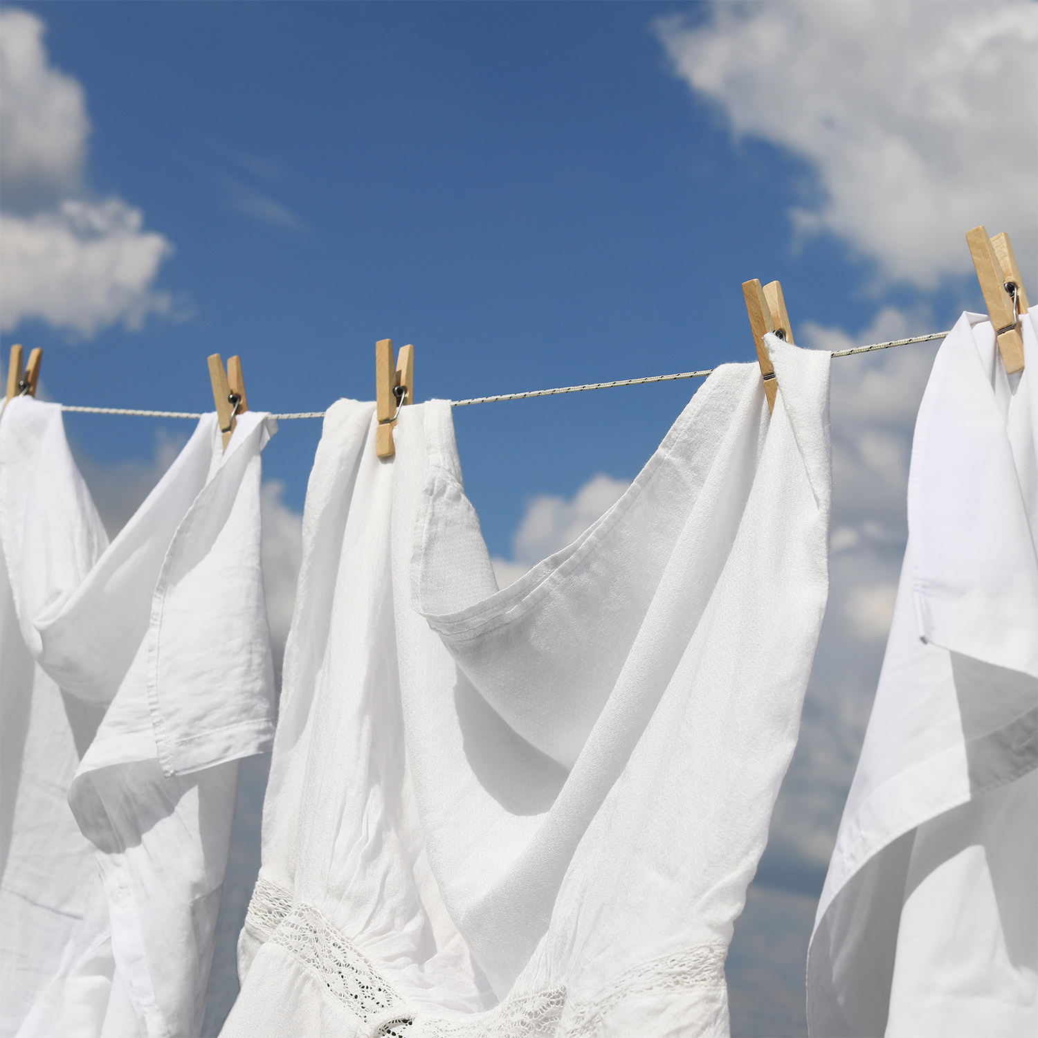 White clothes hang on a line under a blue sky, capturing the fresh aroma of Liberty: American Linen Scented Summer Candle (14 oz) by Tuscany Candle® SEASONAL.