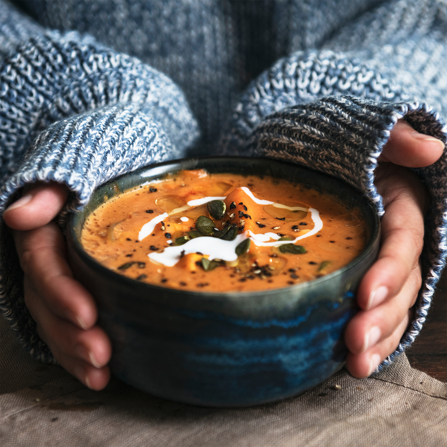 A person in a blue sweater holds a Tuscany Candle® SEASONAL Charmed Pumpkin: Spooky Spice & Pumpkin Scented Halloween Wax Melt (2.5 oz), its creamy orange hue resembling pumpkin soup and artfully garnished with festive details.