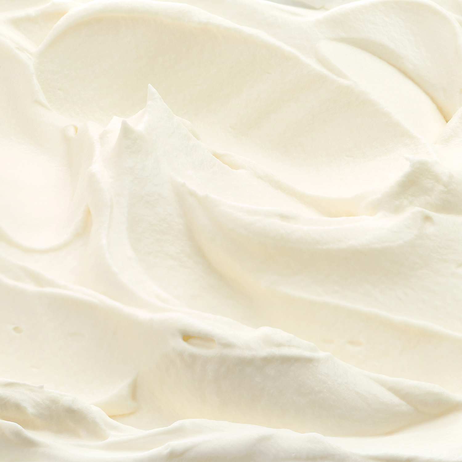 A close-up view of smooth, fluffy whipped cream with soft peaks and swirls, filling the entire frame.