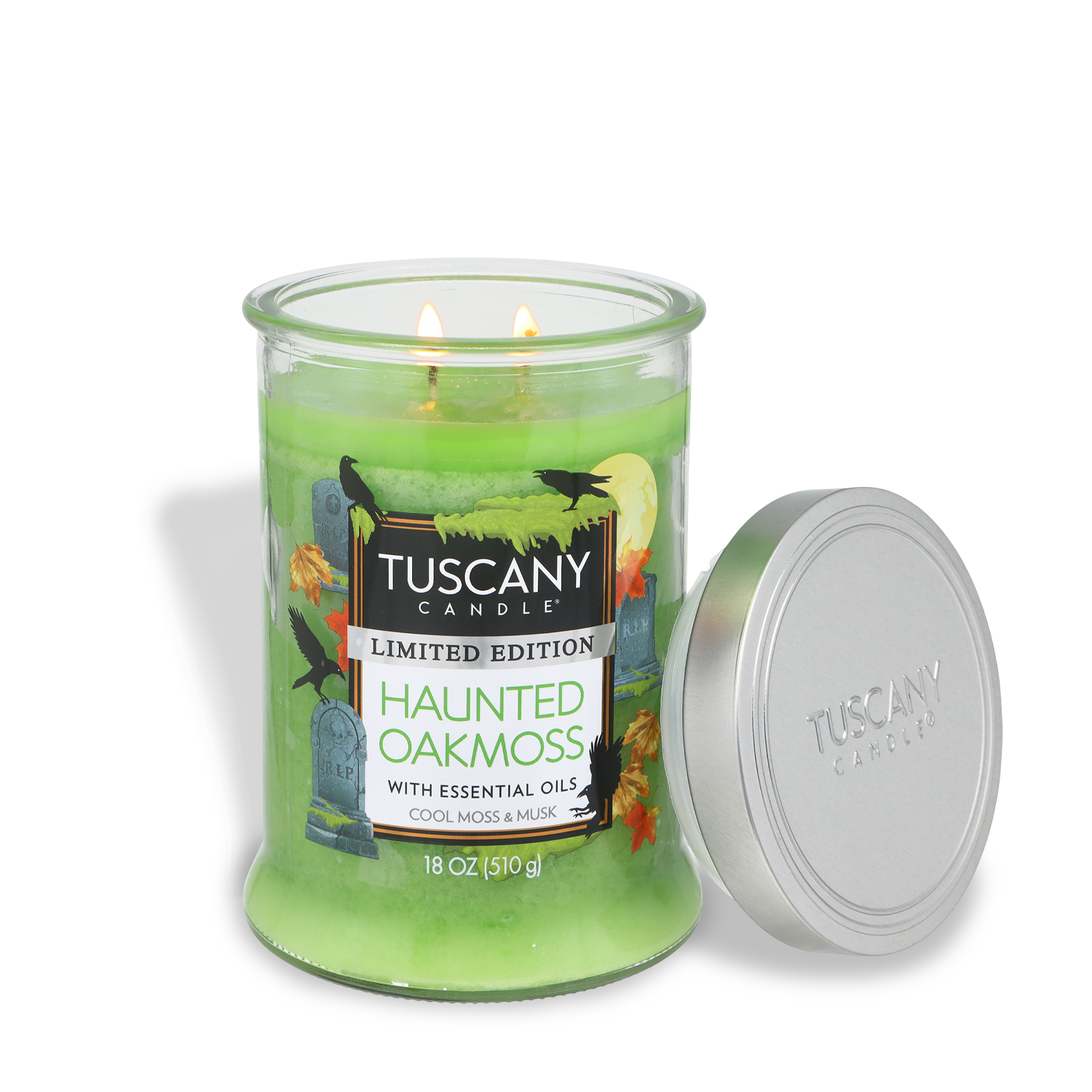 A lit 18 oz Tuscany Candle® SEASONAL jar candle in the “Haunted Oakmoss: Cool Moss & Musk Scent” features Halloween-themed decorations on the label, and a silver lid rests beside the green glass jar.