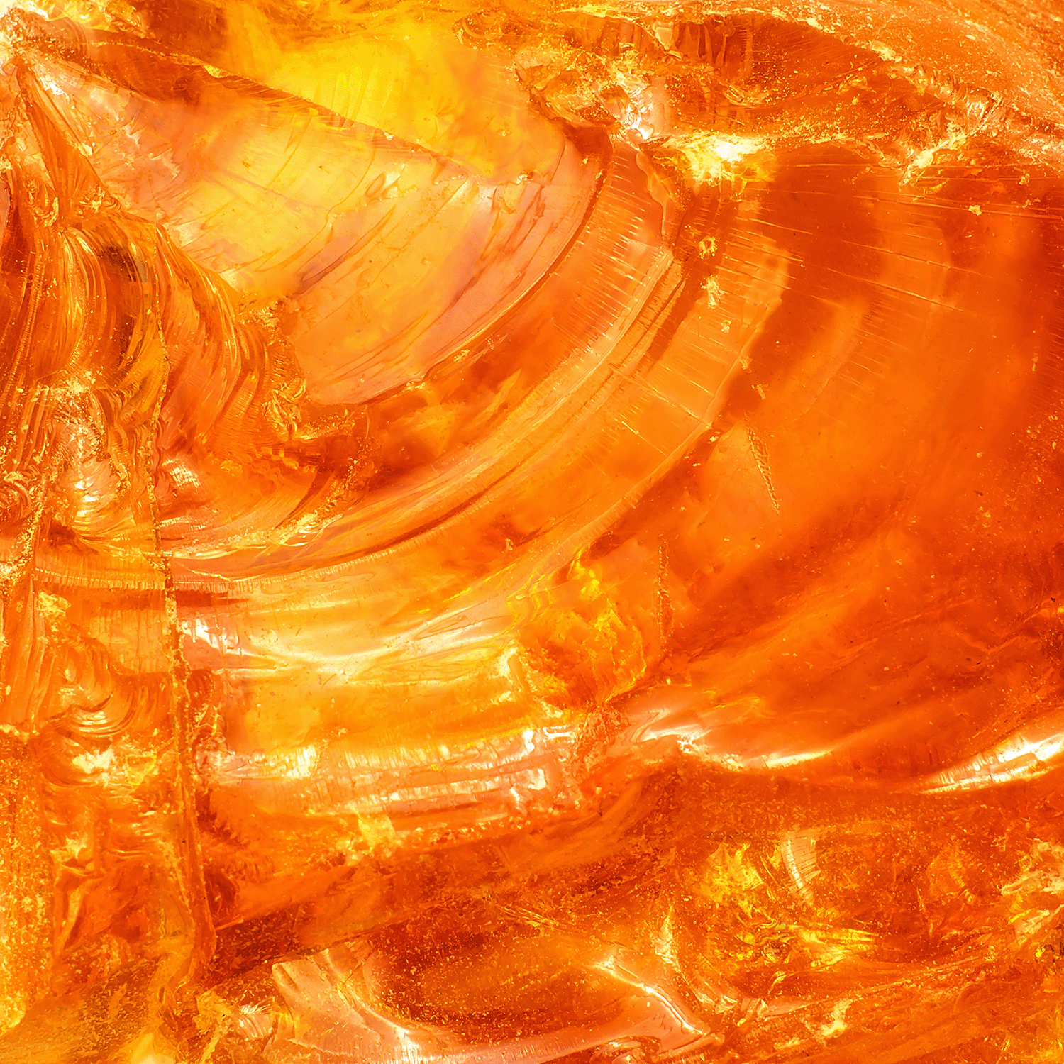 Closeup of the polished surface of the Tuscany Candle® SEASONAL Forbidden Forest: Twilight Amber & Oak Scented Halloween Candle (18 oz), displaying orange and yellow swirling patterns and translucent textures as light shines through.