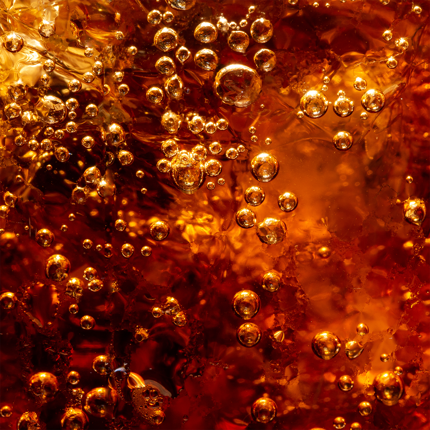 A close-up view of fizzy bubbles rising in a dark amber liquid, reminiscent of a carbonated beverage like soda, with light reflecting through the bubbles and liquid—capturing the essence of Tuscany Candle® SEASONAL’s Spooky Soda: Pumpkin & Cream Soda Scented Halloween Candle (18 oz).