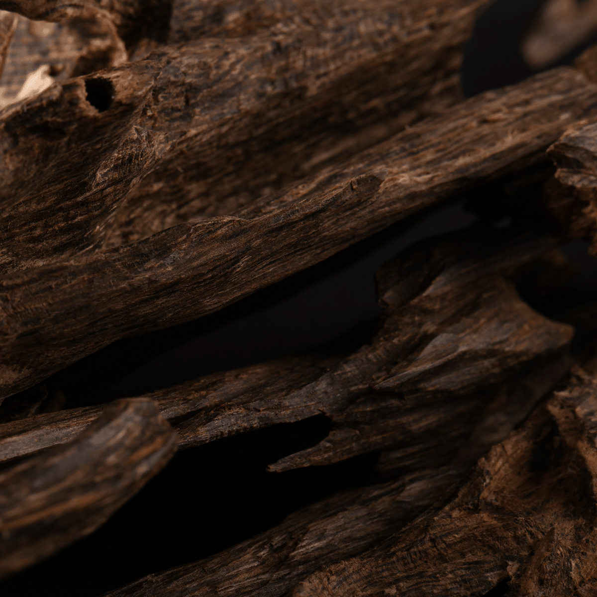 Close-up of the Tuscany Candle® SEASONAL “Full Moon: Black Timber & Red Cherry” scented Halloween candle (12.5 oz), featuring dark brown, textured wax with rough, jagged edges and natural grain patterns, set against a black background.