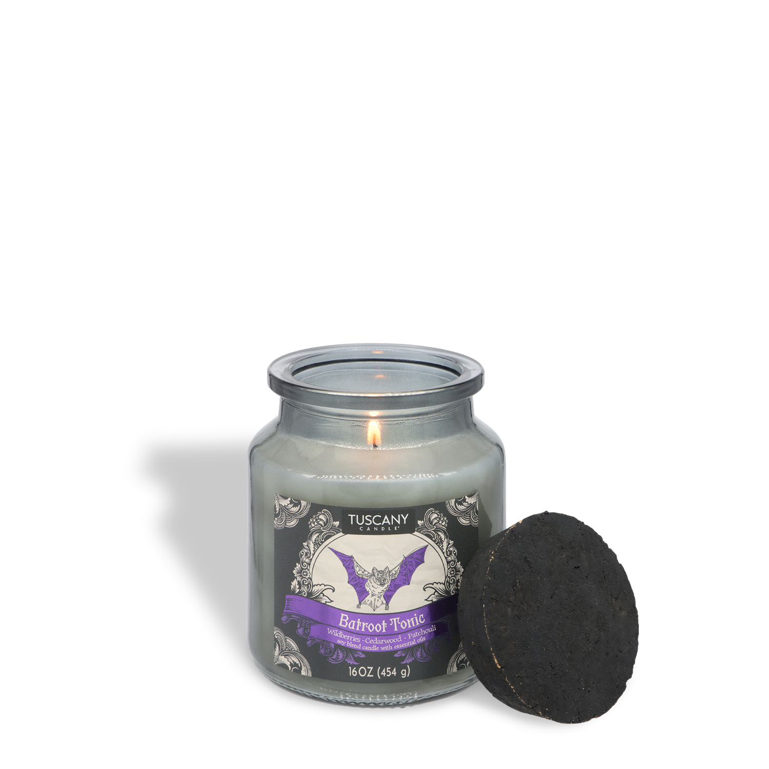 A lit Tuscany Candle® SEASONAL Batroot Tonic: Wildberries & Cedarwood Scented Halloween Candle (16 oz) in a glass jar, labeled “Batroot Tonic,” with a black round object leaning against it, set on a white background.