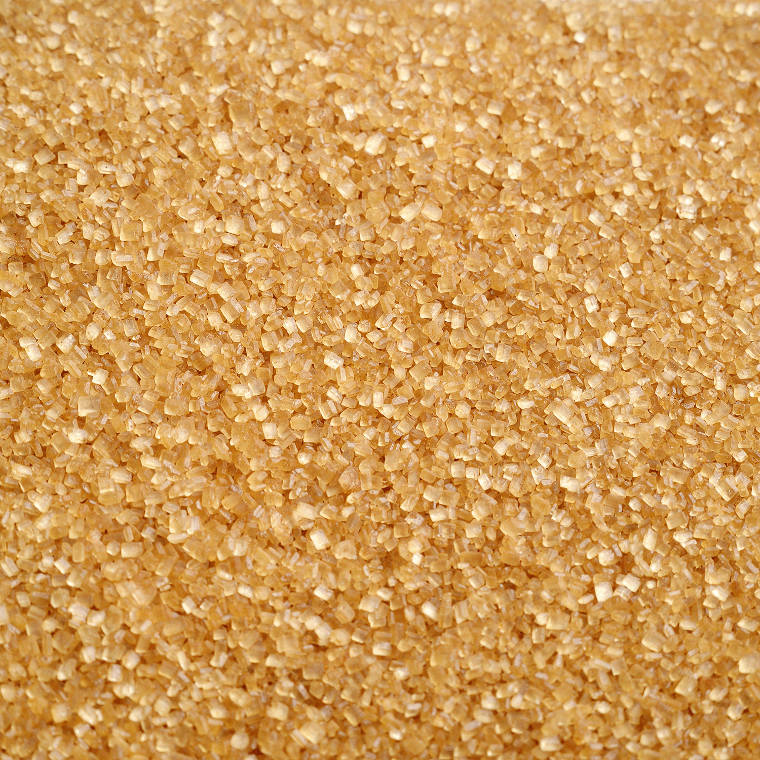 A close-up of irregularly shaped, golden-brown raw sugar crystals offers the perfect inspiration for a cozy autumn home fragrance, such as Tuscany Candle® SEASONAL’s Apple Pie: Cinnamon & Butter Scented Fall Candle (14 oz).