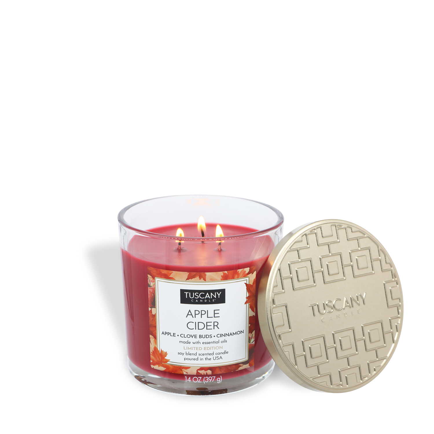A Tuscany Candle® SEASONAL “Apple Cider: Clove Buds & Cinnamon” 14 oz red candle with three lit wicks in a glass jar sits next to a flat gold decorative lid.