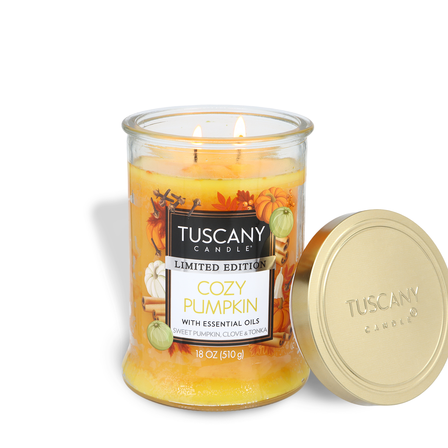 An 18 oz Tuscany Candle® SEASONAL jar labeled "Cozy Pumpkin: Sweet Pumpkin & Clove Scented Fall Candle," with two lit wicks, sits beside its gold lid. The label features autumn decorations.