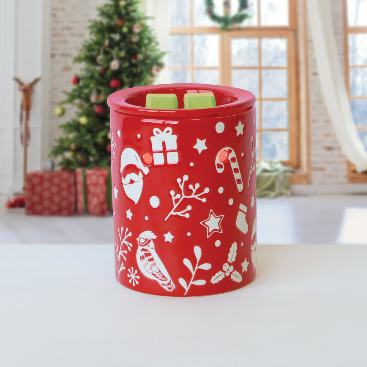 Red holiday-themed wax warmer decorated with white icons of Santa, gifts, and birds, containing two green Winter Pear: Golden Pear & Vanilla Scented Holiday Wax Melt (2.5 oz) cubes.