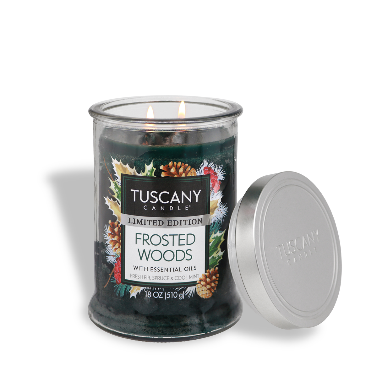 A lit two-wick Tuscany Candle® SEASONAL Frosted Woods: Fresh Fir & Spruce Scented Holiday Candle (18 oz) in a glass jar with a pine-and-holly label, shown with its silver lid removed.
