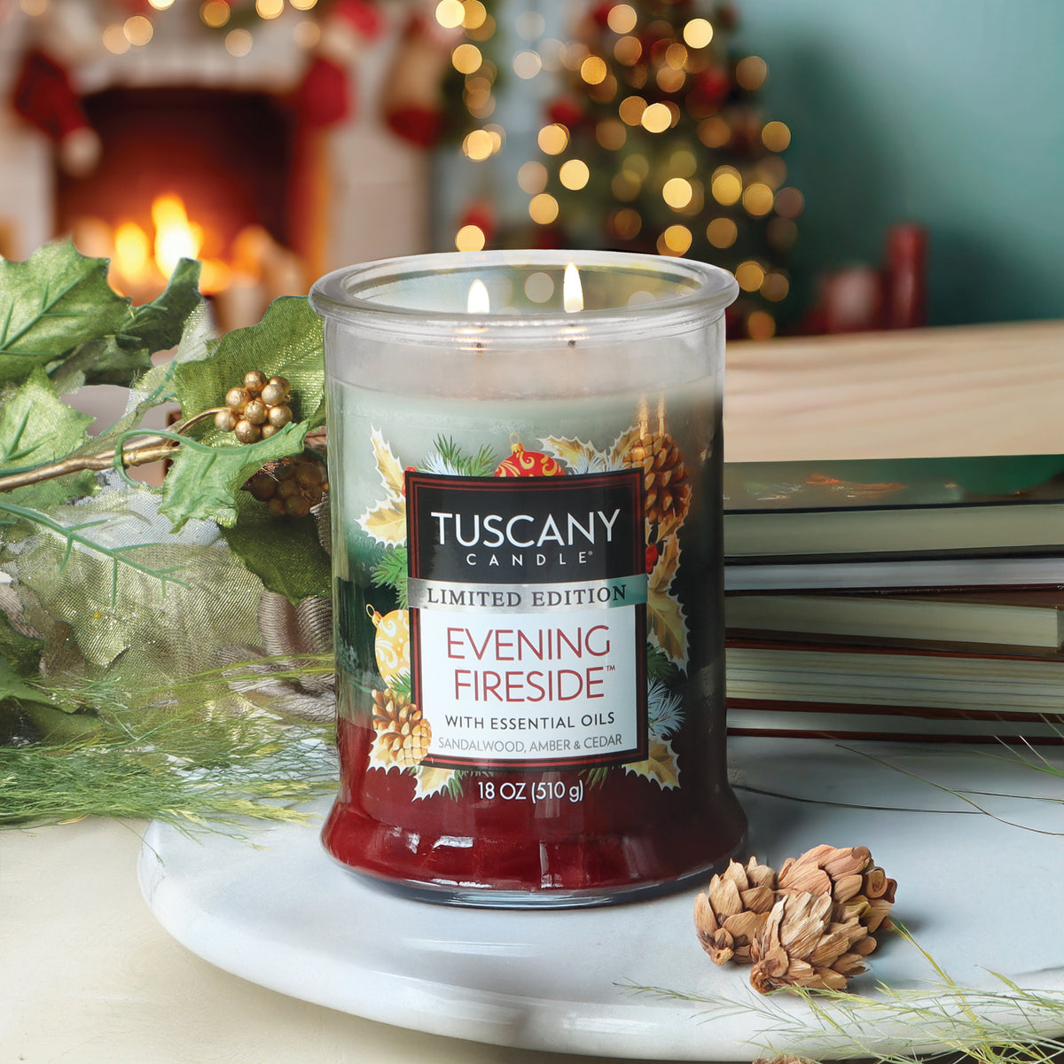 An 18 oz Evening Fireside®: Sandalwood & Amber Scented Holiday Candle by Tuscany Candle® in a two-wick glass jar with a pinecone and ornament label, set on a stone tray.