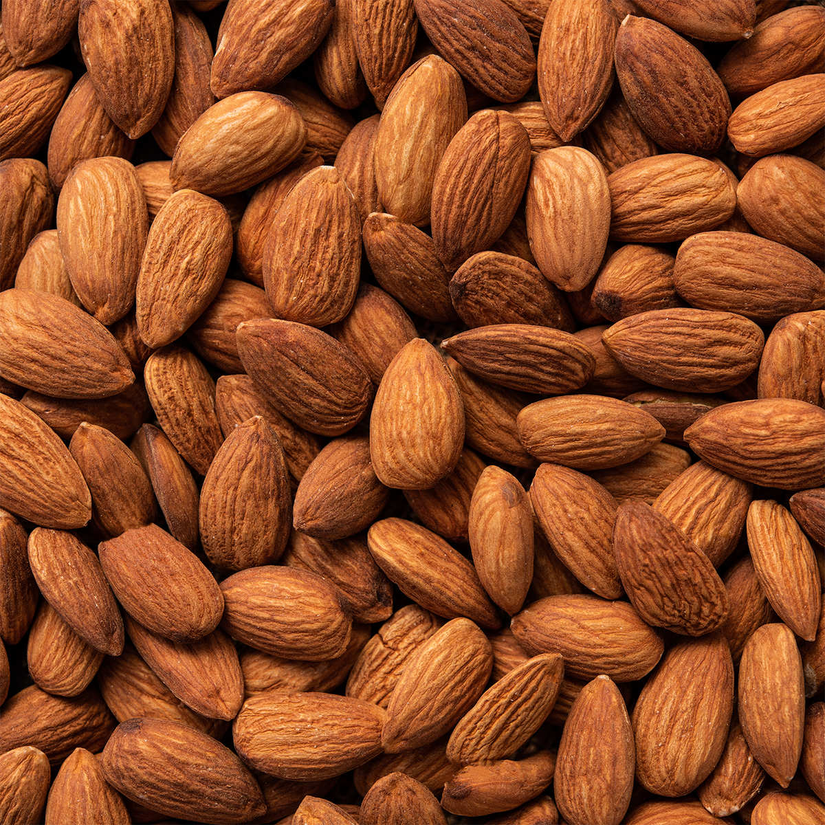 A close-up, top-down view of many whole almonds filling the frame, accompanying a Santa’s Bakeshop: Almond & Vanilla Scented Holiday Candle (18 oz).