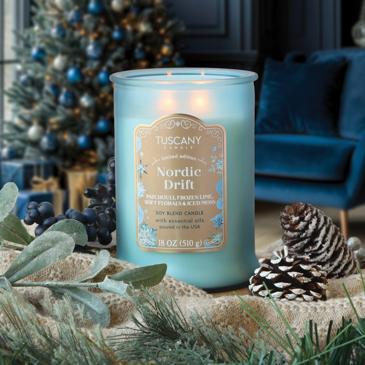 A Nordic Drift: Frozen Lime & Patchouli Scented Holiday Candle in a light blue, two-wick glass jar, surrounded by pine cones and holiday greenery.