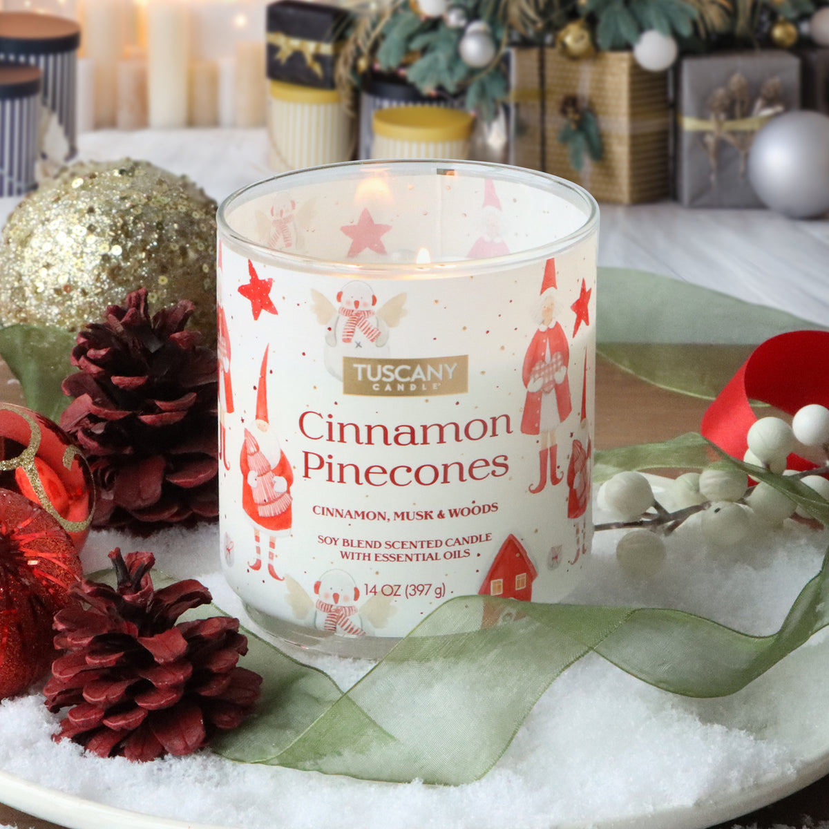 A Tuscany Candle® SEASONAL Cinnamon Pinecones: Cinnamon & Musk Scented Holiday Candle (14 oz) with a gnome-themed label, surrounded by pinecones, red ornaments, and faux snow.