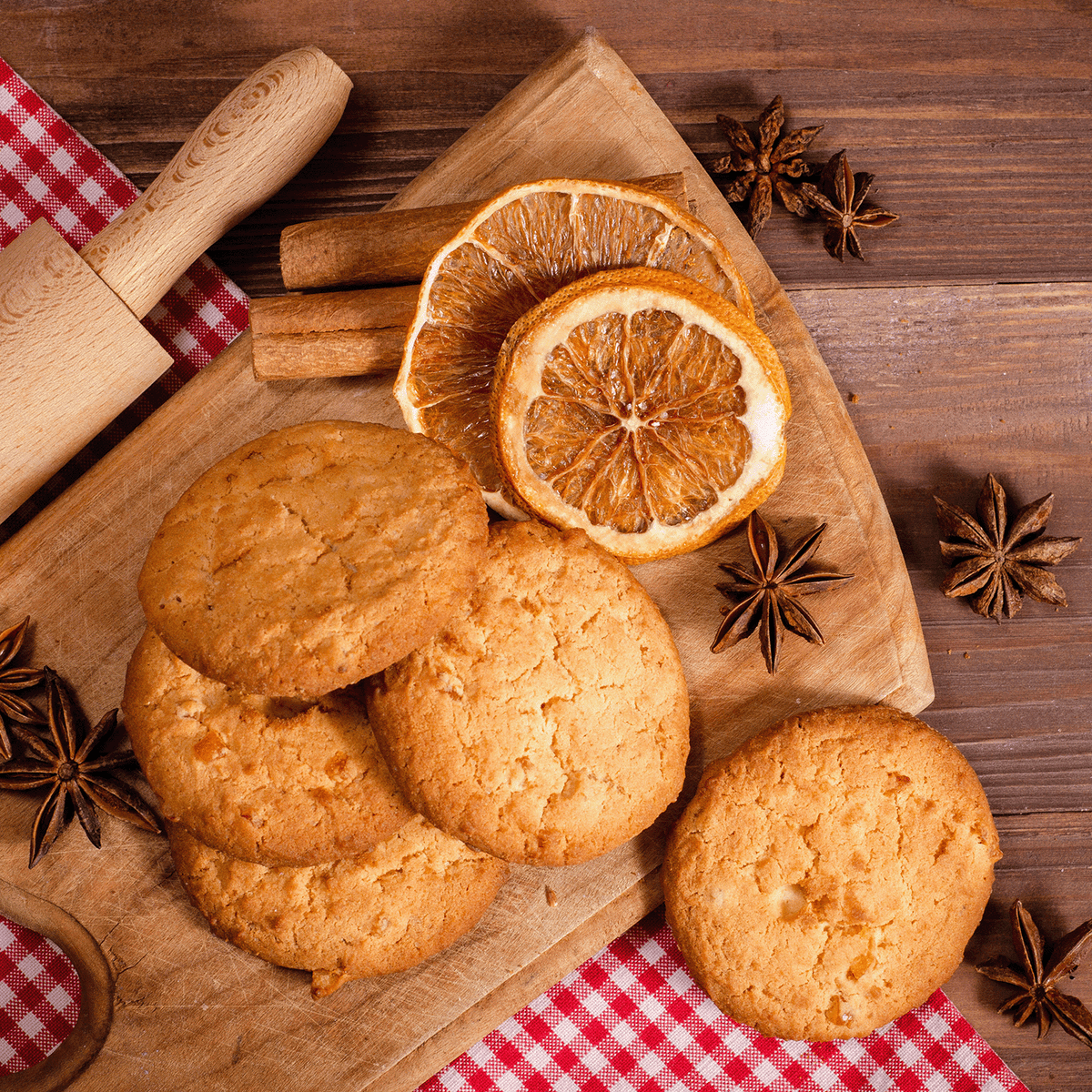 A stack of round Cranberry Shortbread: Baked Vanilla & Butter Scented Holiday Candle (14 oz) shortbread cookies on a wooden cutting board with dried orange slices, cinnamon sticks, and star anise.