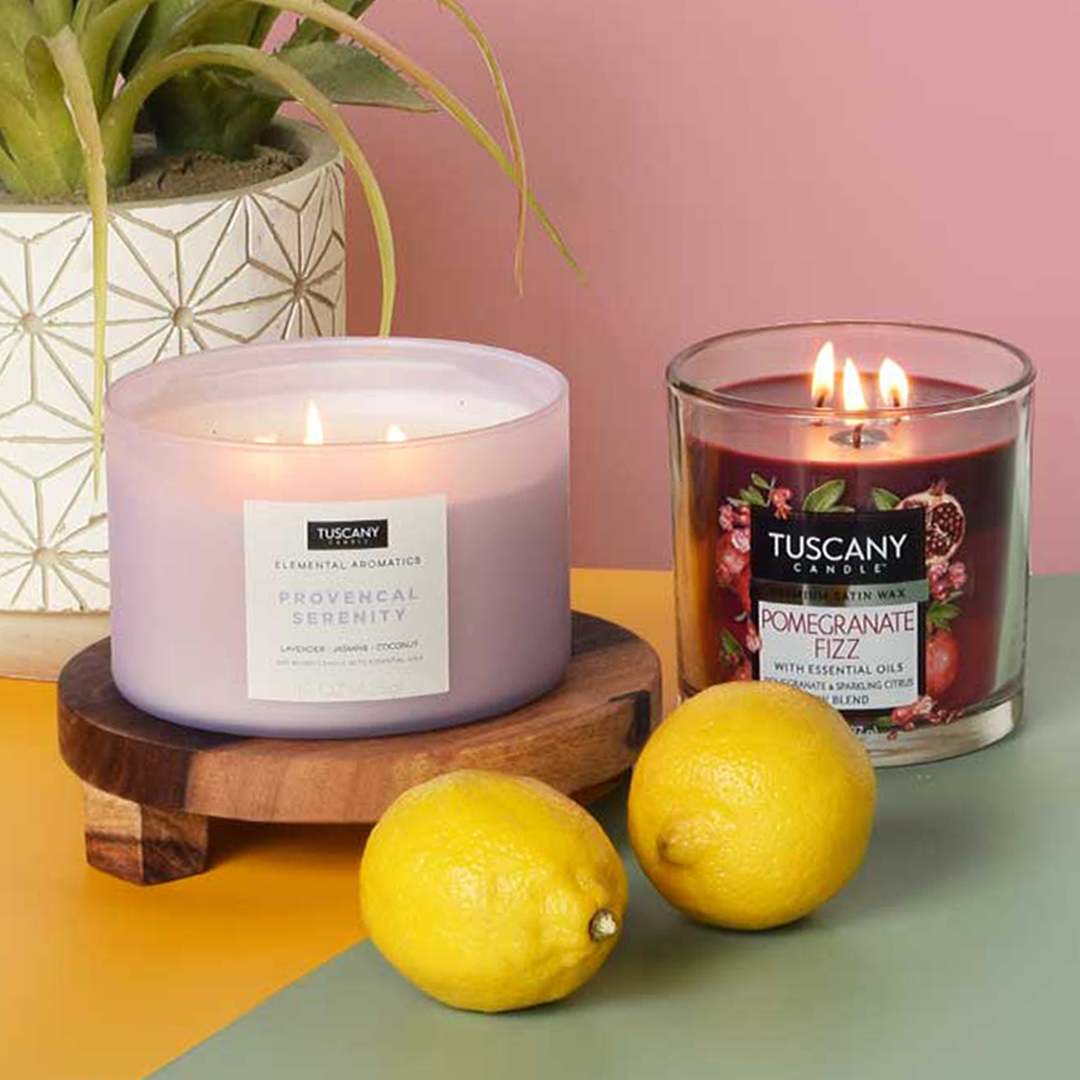 A Pomegranate Fizz Long-Lasting Scented Jar Candle (14 oz) by Tuscany Candle with fragrance notes of pomegranate fizz and a lemon next to it.