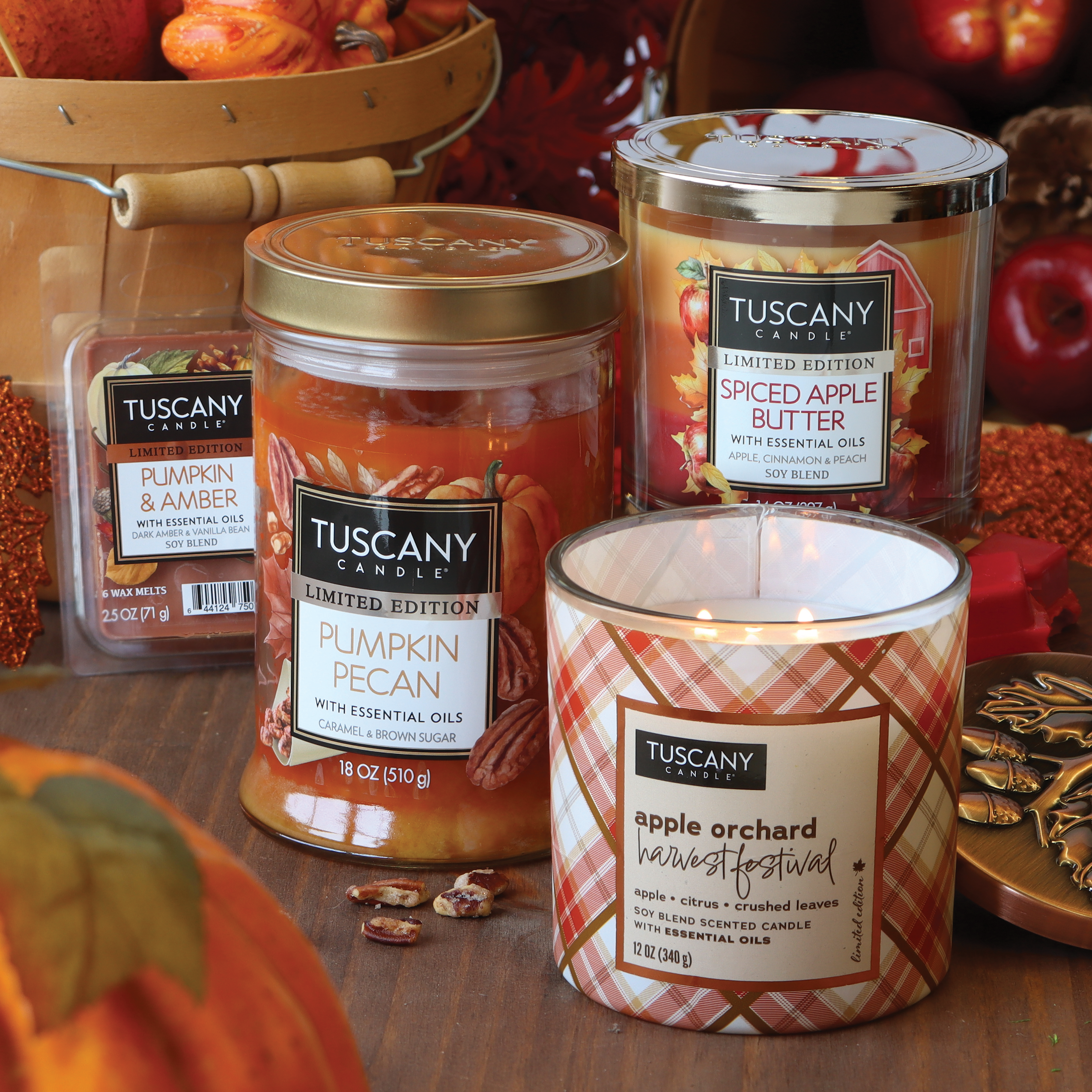 A collection of Tuscany candles, including Pumpkin Pecan, Spiced Apple Butter, Pumpkin & Amber, and a lit Tuscany Candle® SEASONAL Apple Orchard Harvest Festival Long-Lasting Scented Jar Candle (12 oz) from the Autumn Flannels Collection, displayed on a wooden surface with autumn leaves and fall decorations.