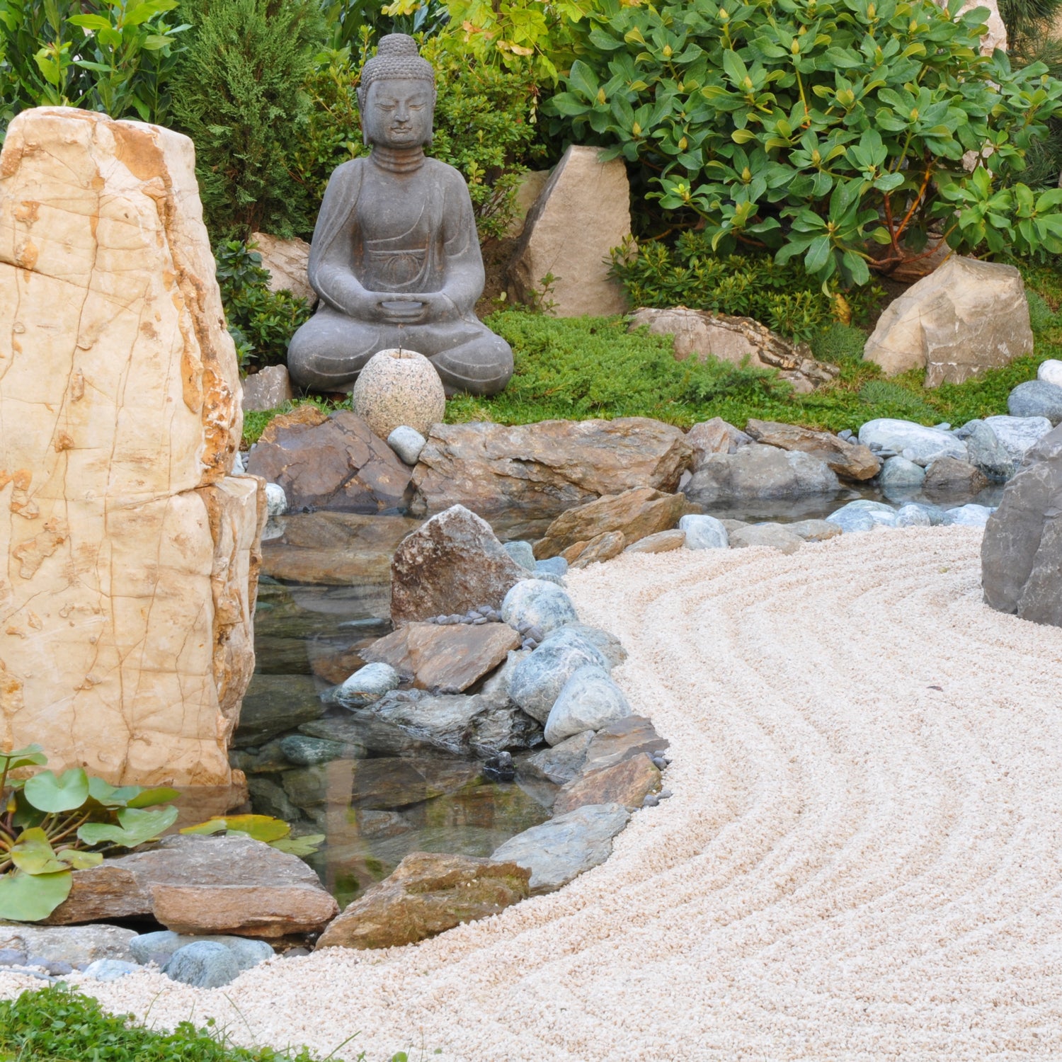 A serene Zen Garden Scented Jar Candle (14 oz) from the Tuscany Candle Home Décor Collection, adorned with rocks, where a peaceful buddha statue resides.