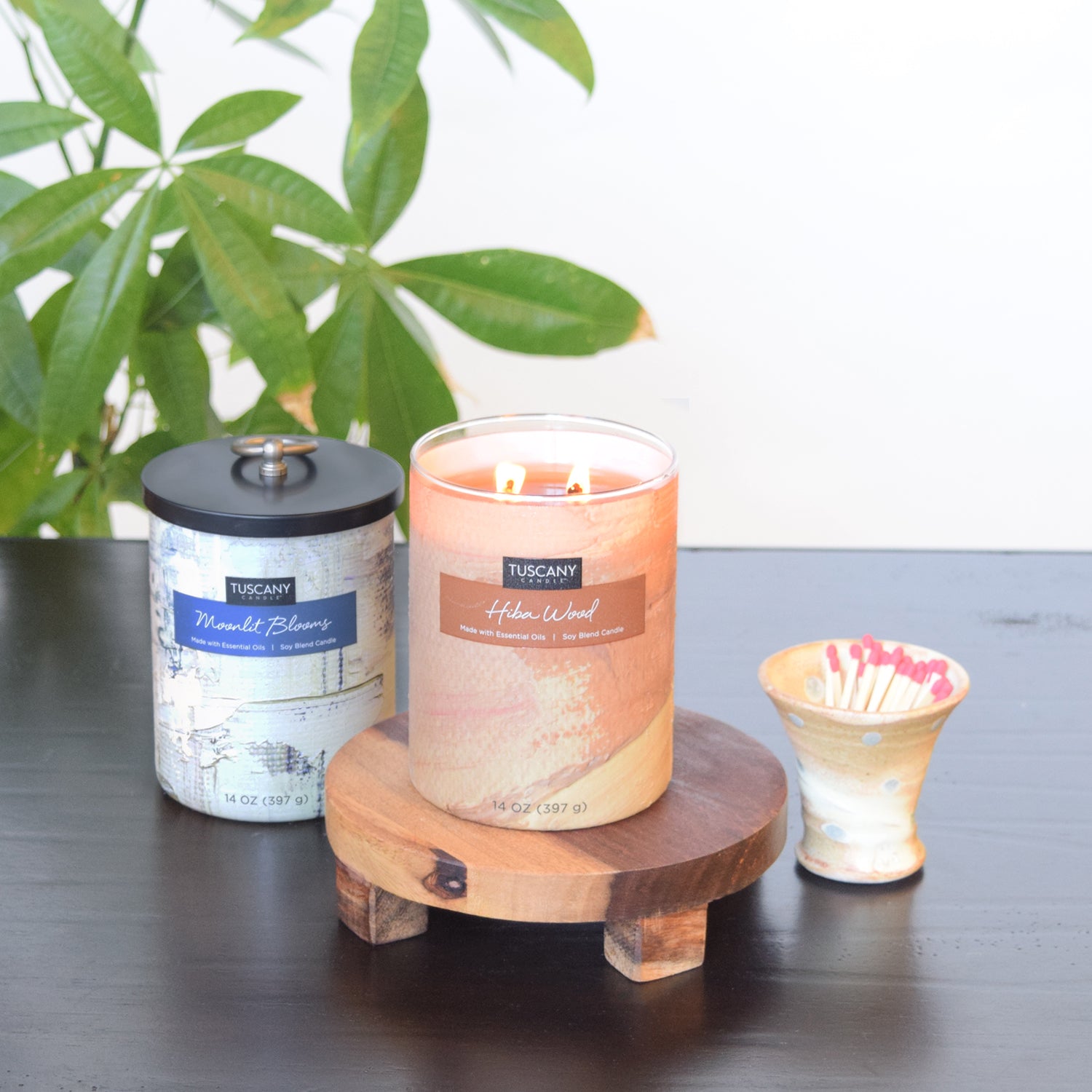 A Moonlit Blooms Scented Jar Candle (14 oz) – Home Décor Collection sits on a wooden table next to a plant.