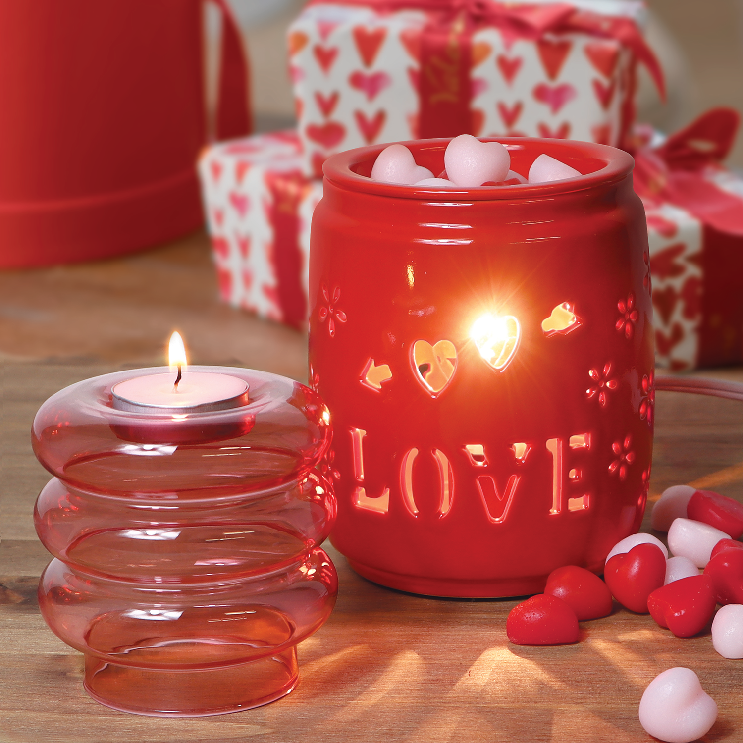 A Tuscany Candle® SEASONAL scented candle in a red jar next to a box of candy.