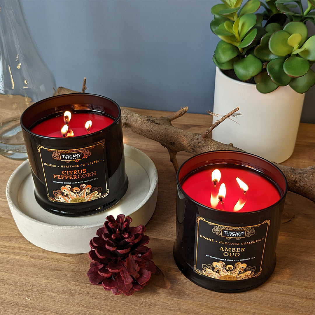 Two tins of Citrus Peppercorn Scented Jar Candle (15 oz) – Homme + Heritage Collection by Tuscany Candle on a table next to a plant.