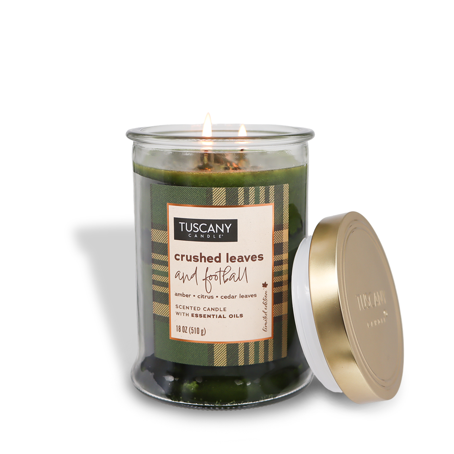 Tuscany Candle® SEASONAL's Crushed Leaves and Football Long-Lasting Scented Jar Candle (18 oz) from the Autumn Flannels Collection, featuring aromatic notes of amber, citrus, and crushed cedar leaves, sits with its gold lid off to the side. The candle boasts two wicks lit in a stylish glass jar.