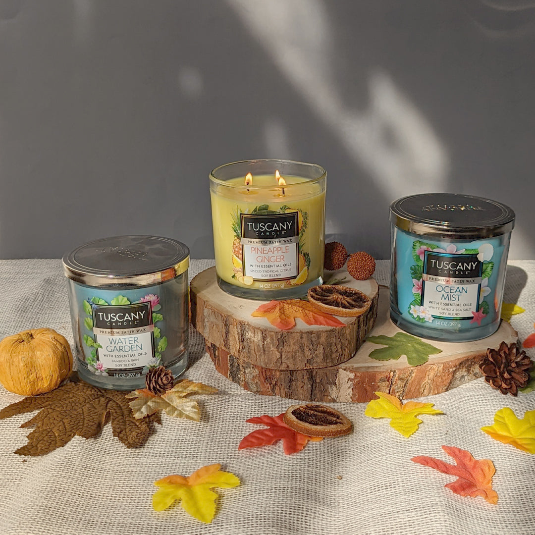 Three Pineapple Ginger Long-Lasting Scented Jar Candles (14 oz) by Tuscany Candle sitting on top of a table with fall leaves emit a mesmerizing fragrance.
