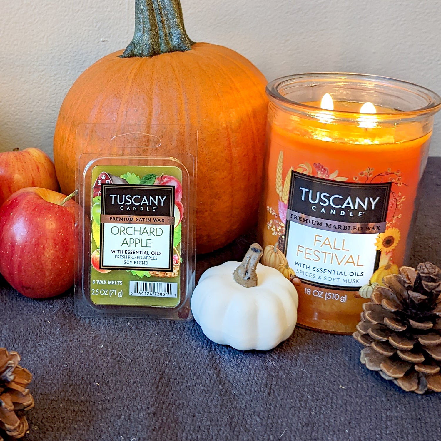 Fall inspired scented candles and tart bars are shown in a still life with pumpkins and apples