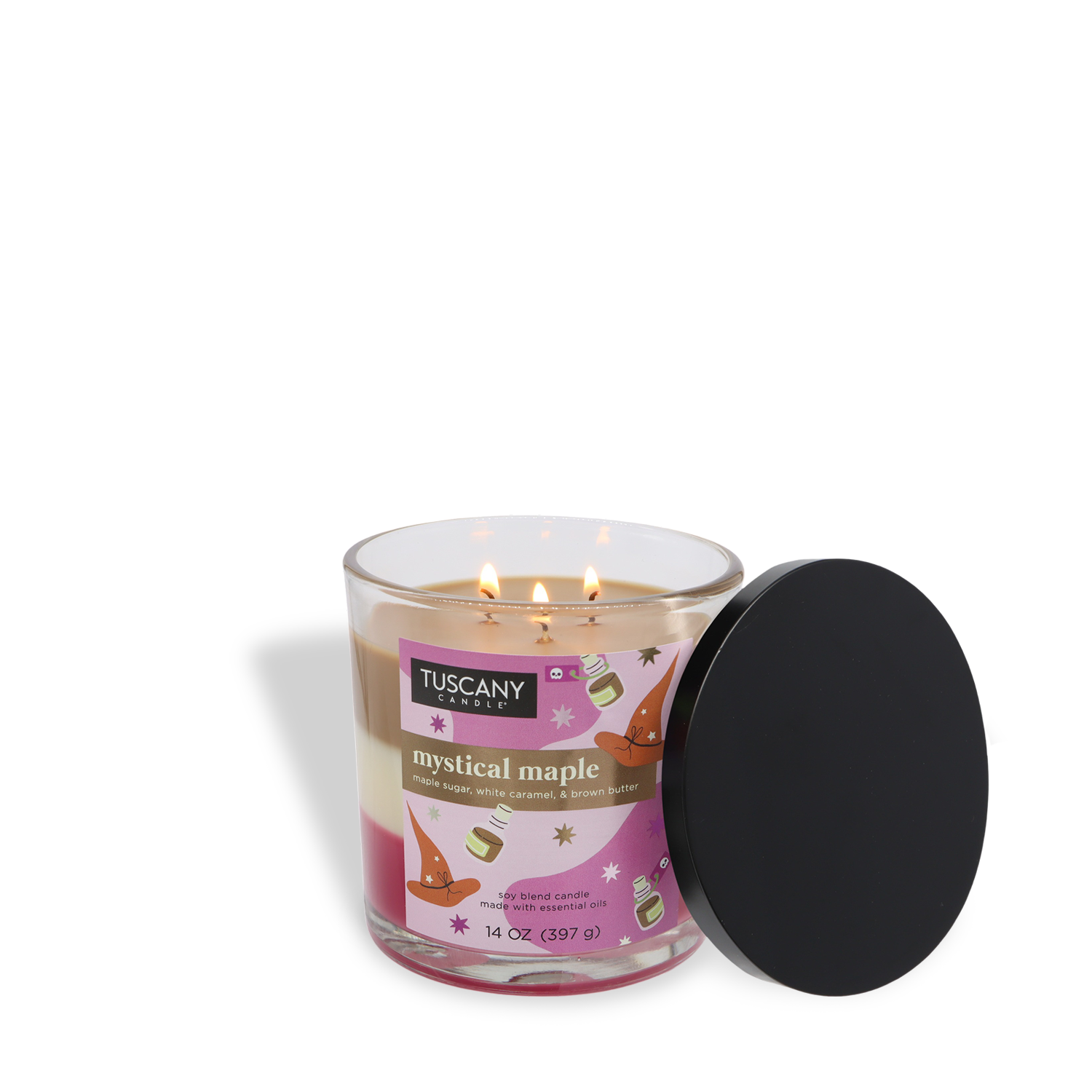 A 14 oz glass jar candle labeled "Mystical Maple: Sweet Molasses & Brown Butter" by Tuscany Candle® SEASONAL, with two lit wicks and a black lid resting on the side.