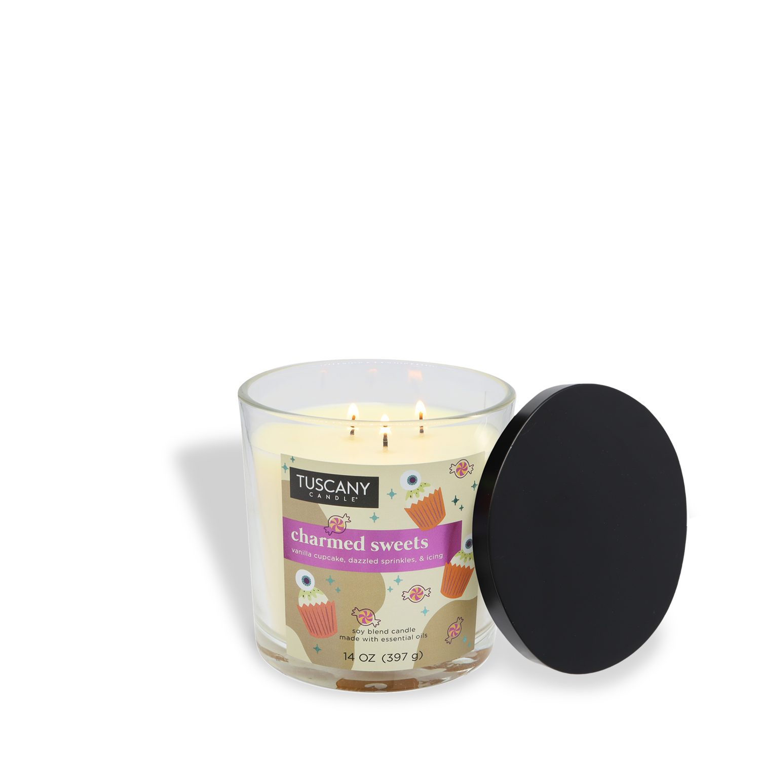 A lit Tuscany Candle® SEASONAL "Charmed Sweets: Vanilla Cupcake & Buttercream Icing" Halloween candle (14 oz) in a glass jar, with its black lid resting beside it.