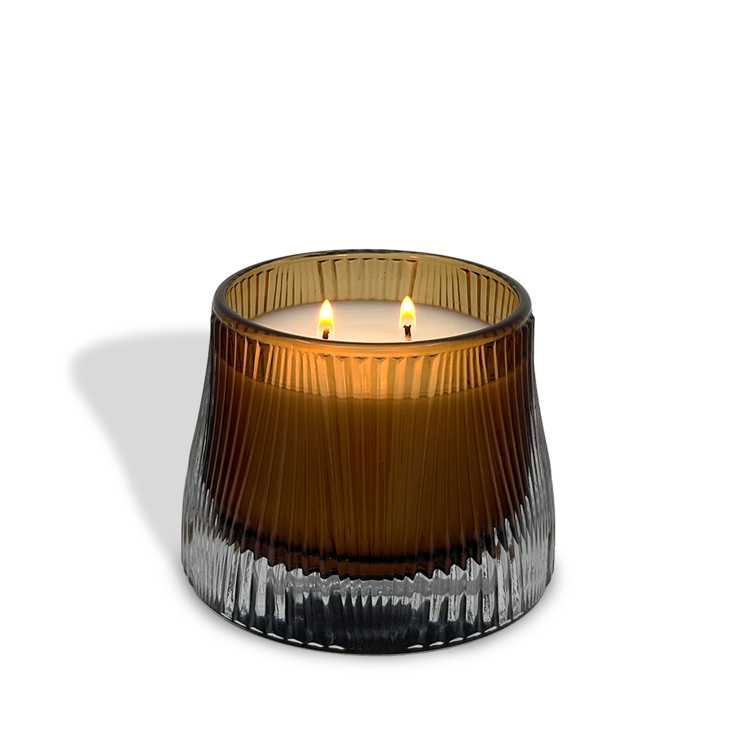 The est.1951 Sandalwood & Ginger (9oz) candle glows with two wicks in a ribbed, translucent brown glass container, casting shadows on a white background.