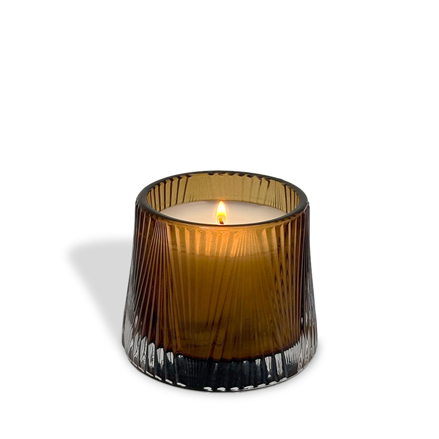The est.1951 Sandalwood & Ginger 4oz candle, in a ribbed translucent brown glass holder, sits on a white surface, its ginger scent wafting as it casts a soft shadow to the left.