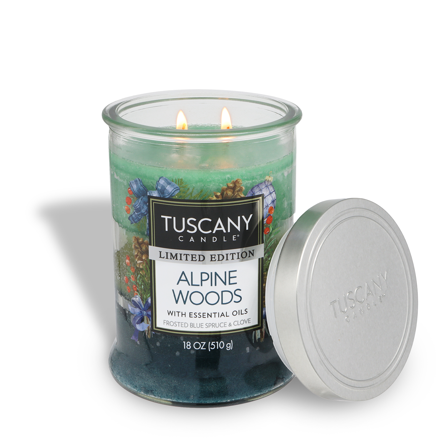 A green and blue glass jar candle labeled “Tuscany Candle® SEASONAL Alpine Woods: Frosted Blue Spruce Scented Holiday Candle (18 oz),” with two lit wicks beside its silver lid; marked as limited edition.
