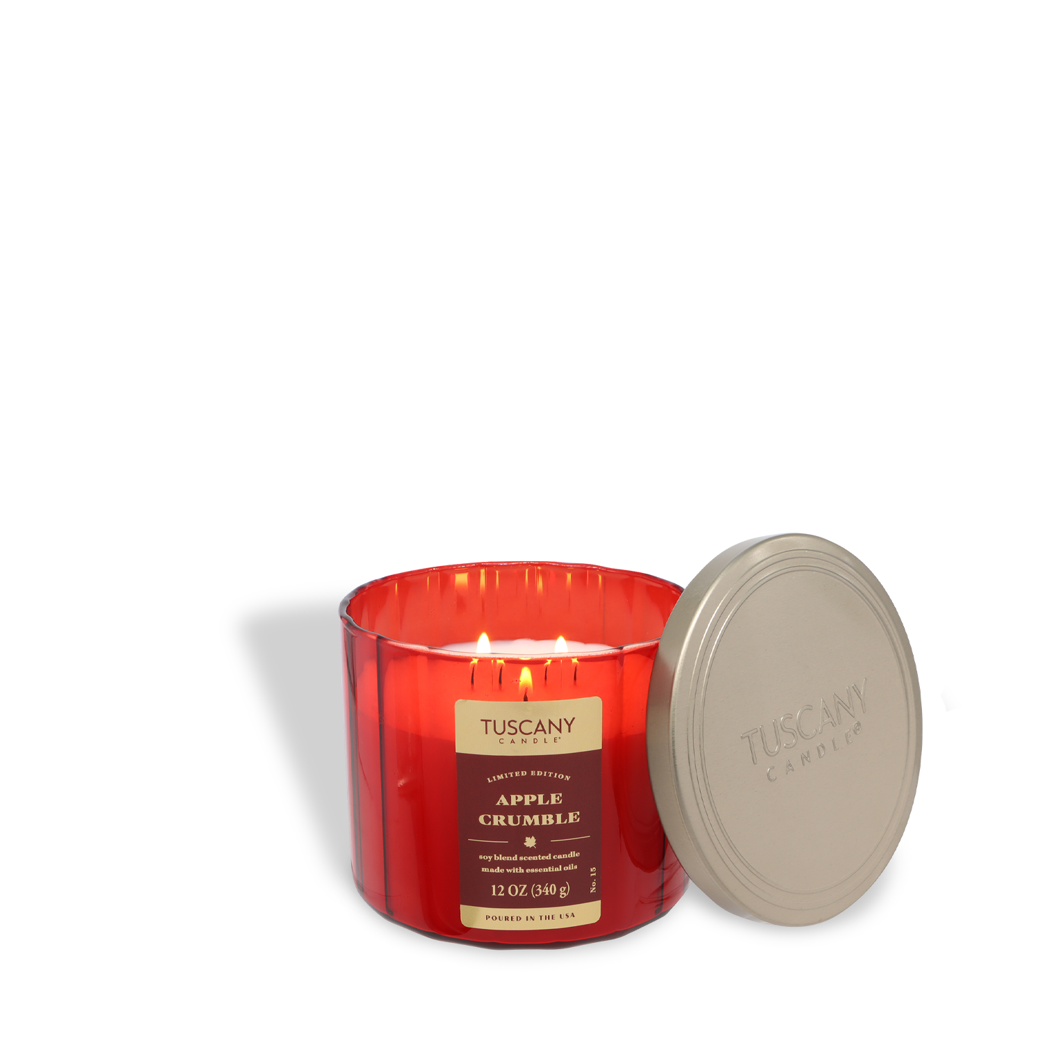 A Tuscany Candle® SEASONAL Apple Crumble: Cinnamon & Buttercream Scented Fall Candle (12 oz) glows in a red jar labeled "Apple Crumble," with its gold lid placed beside it.
