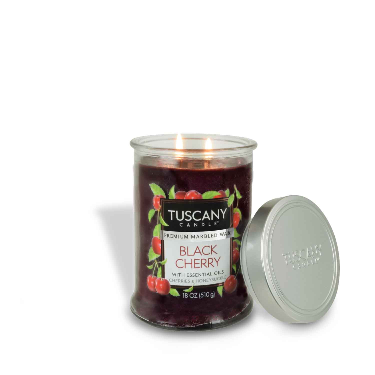 An 18 oz Black Cherry Long-Lasting Scented Jar Candle by Tuscany Candle® EVD, adorned with cherry illustrations and essential oils, sits lit with its silver lid beside it.