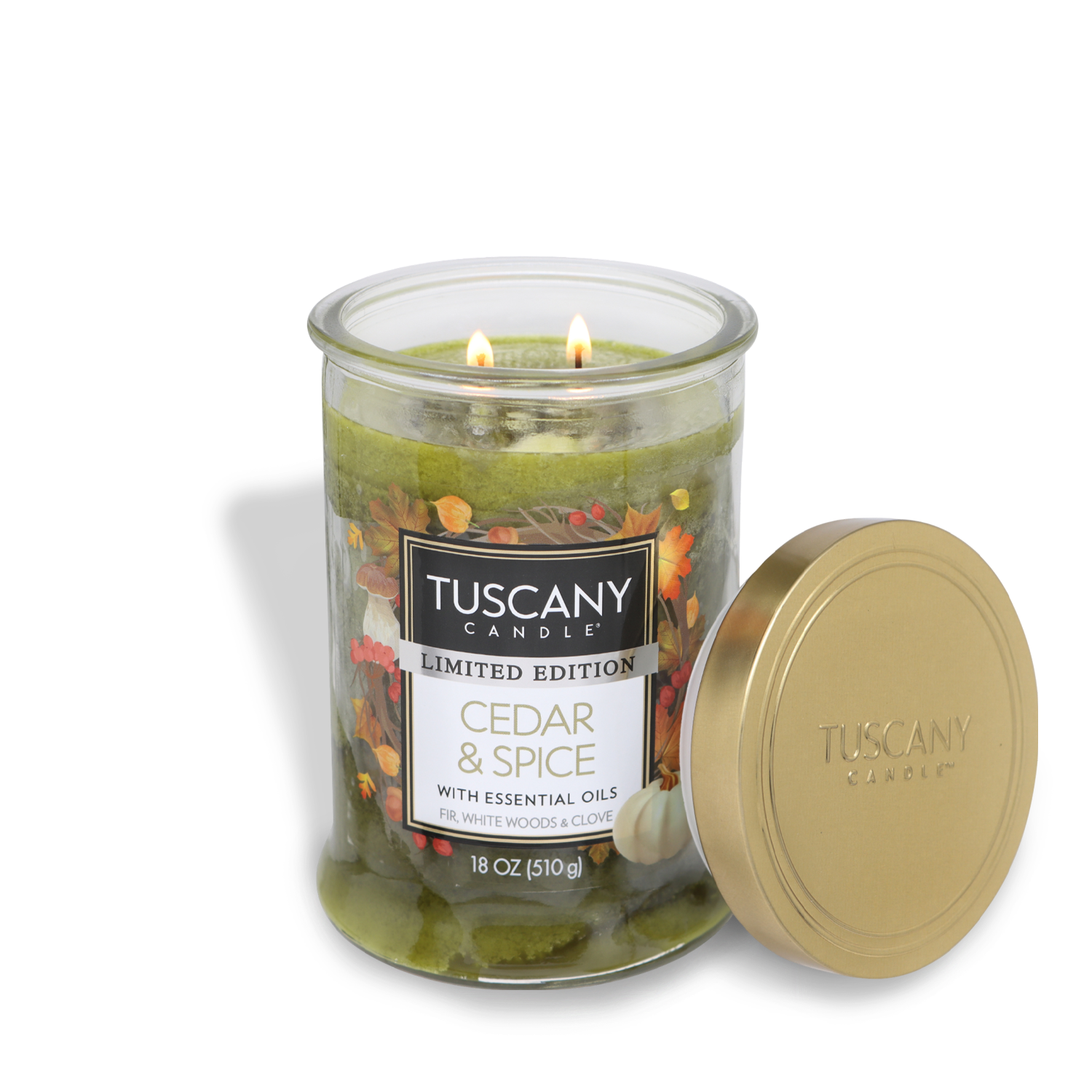 An 18 oz Tuscany Candle® SEASONAL labeled "Cedar & Spice Long-Lasting Scented Jar Candle" with essential oils, featuring two lit wicks. The scented candle comes in a clear glass jar with a gold lid beside it. Limited Edition is noted on the label.