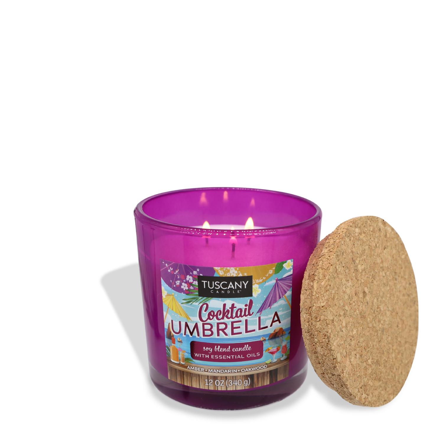 A purple Tuscany Candle® SEASONAL labeled "Cocktail Umbrella (12 oz) – Sunset Beach Bar Collection" with essential oils is lit. Notes of mandarin and oakwood mingle in the air, while the candle's cork lid is placed beside it.