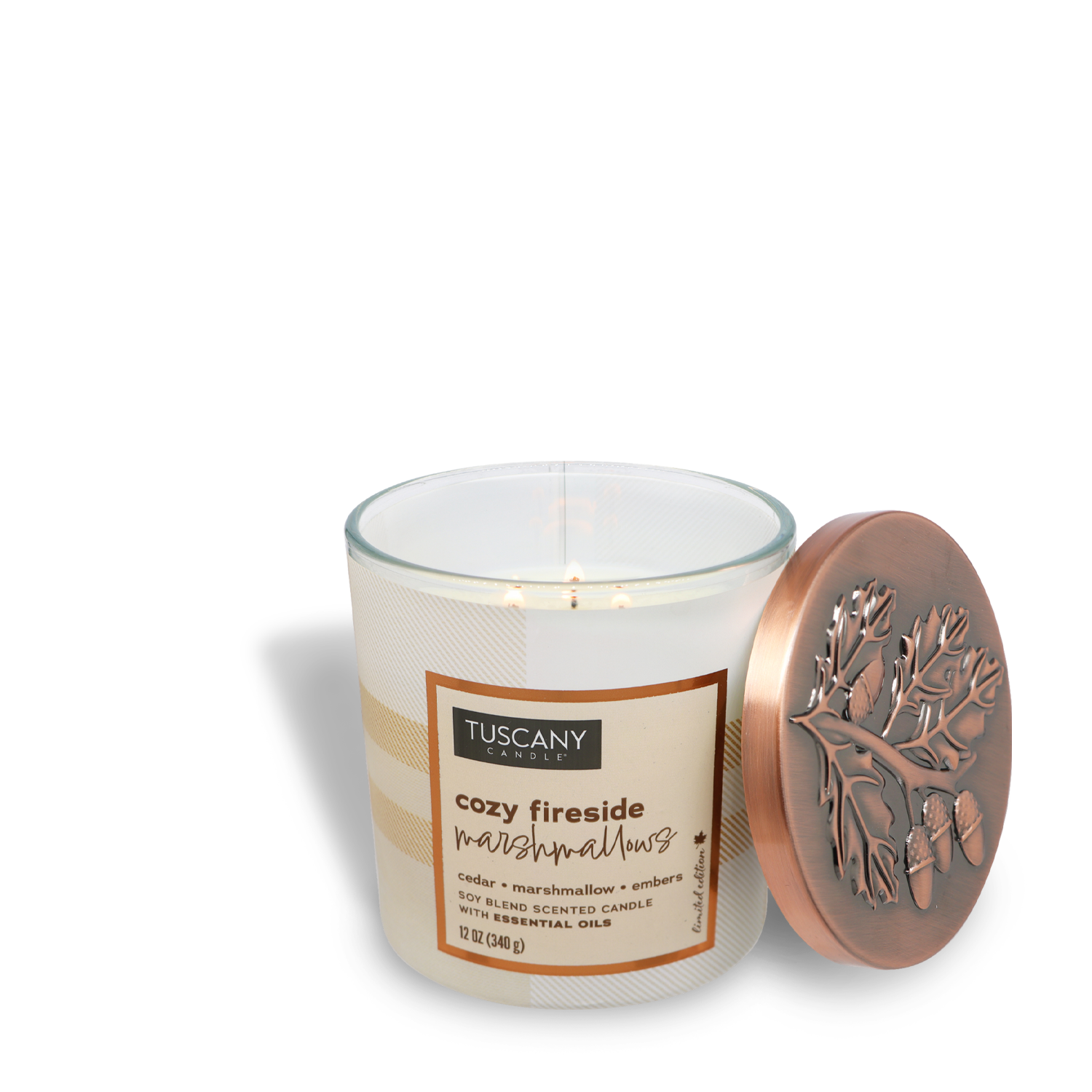 A lit scented candle labeled "Cozy Fireside Marshmallows Long-Lasting Scented Jar Candle (12 oz)" by Tuscany Candle® SEASONAL, part of the Autumn Flannels Collection, in a glass jar with a decorative lid placed beside it. The candle has three wicks and features scent notes of a warm cedar woodsy aroma.