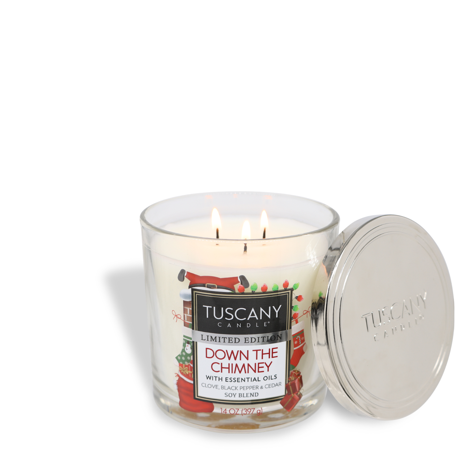 A lit Tuscany Candle® SEASONAL "Down The Chimney" Long-Lasting Scented Jar Candle (14 oz), placed next to its lid. The label mentions essential oils and a scent blend of clove, blackberry, and cedar.