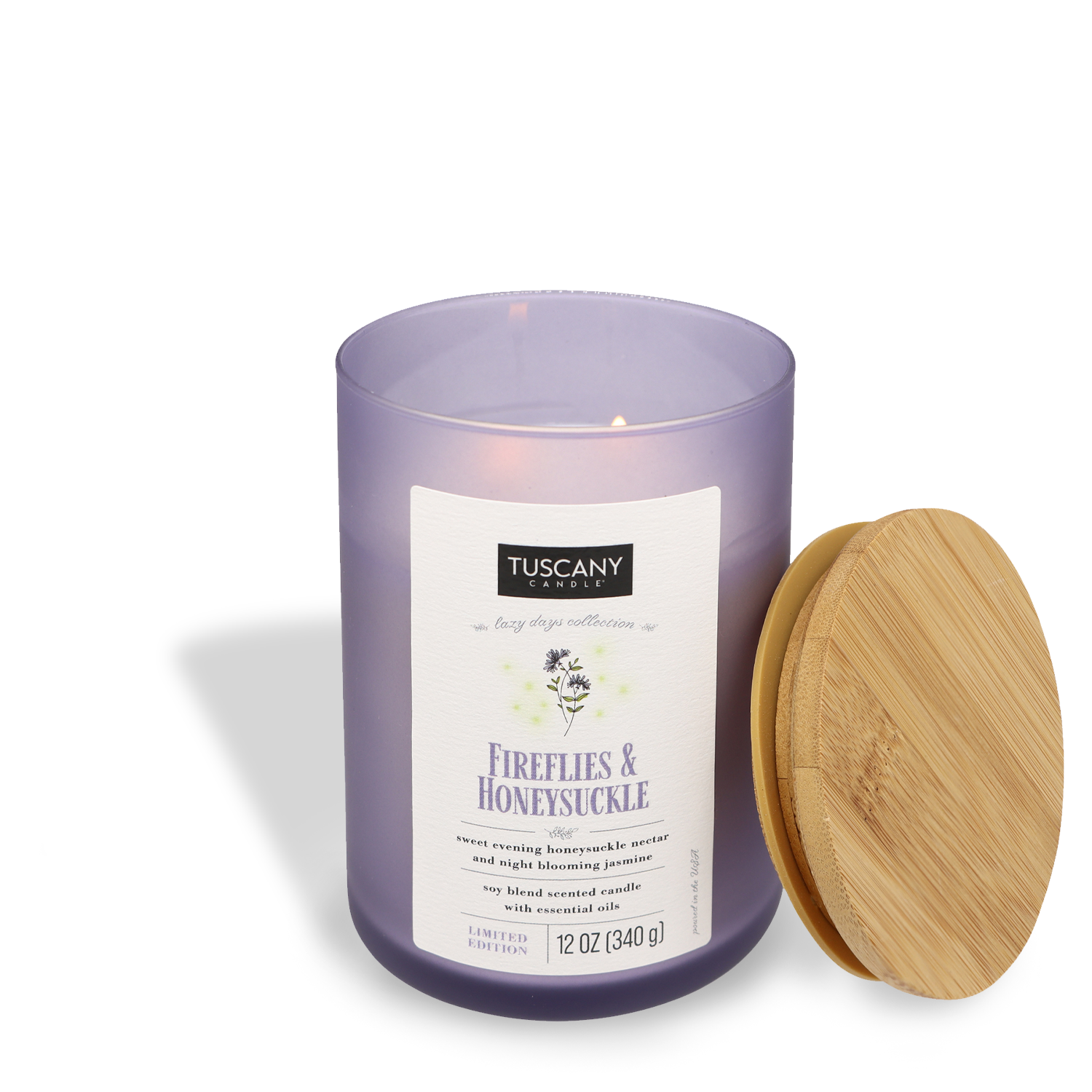 A lavender-colored Tuscany Candle® SEASONAL labeled "Fireflies & Honeysuckle (12 oz) – Lazy Days Collection" with a wooden lid beside it.