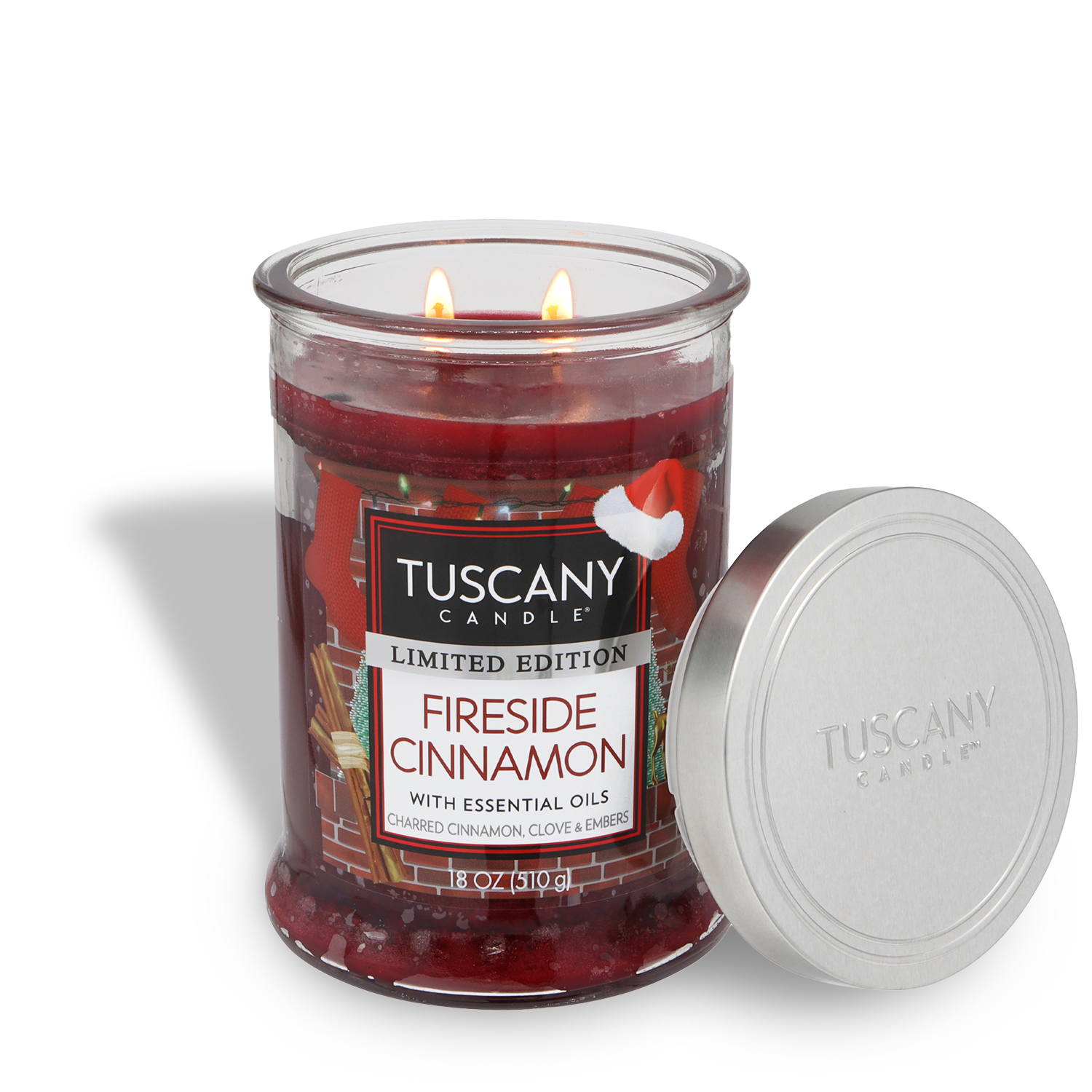 A Tuscany Candle® SEASONAL "Fireside Cinnamon: Charred Clove & Embers" 18 oz candle with two lit wicks and a silver lid sits beside the jar.
