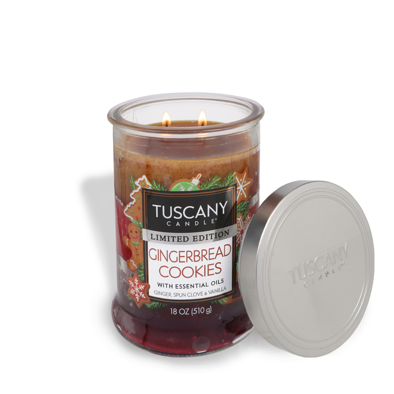 A lit Gingerbread Cookies Long-Lasting Scented Jar Candle (18 oz) by Tuscany Candle® SEASONAL, with its lid placed on its side. The label indicates it contains essential oils and weighs 18 oz (510 g).