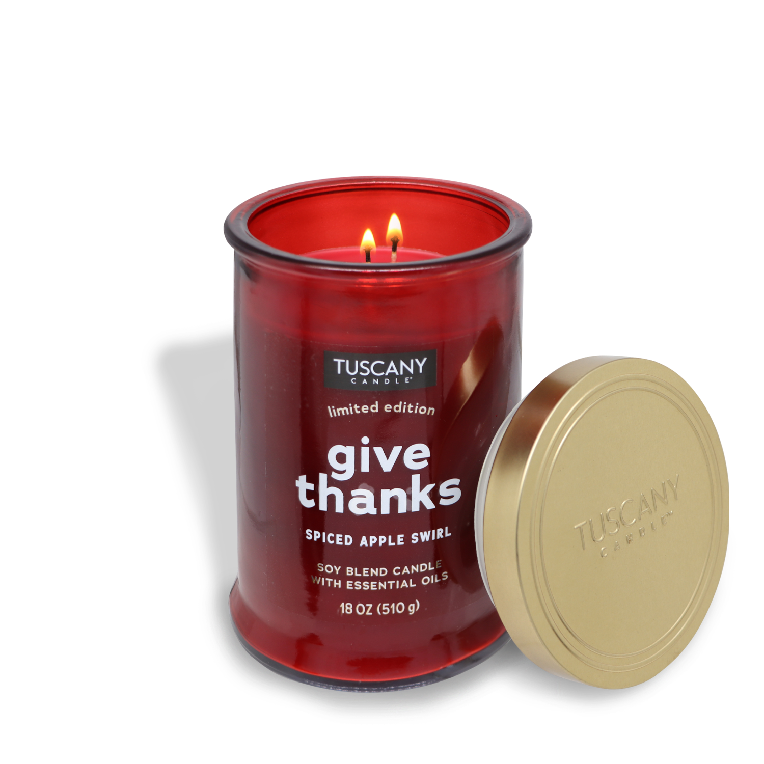 A Tuscany Candle® SEASONAL from the Gather Together Collection, labeled "Give Thanks," has been lit with two wicks, filling the air with its spiced apple swirl fragrance. This 18 oz. red jar candle hints at notes of cinnamon and brown sugared apples, while its gold-colored lid rests beside it.