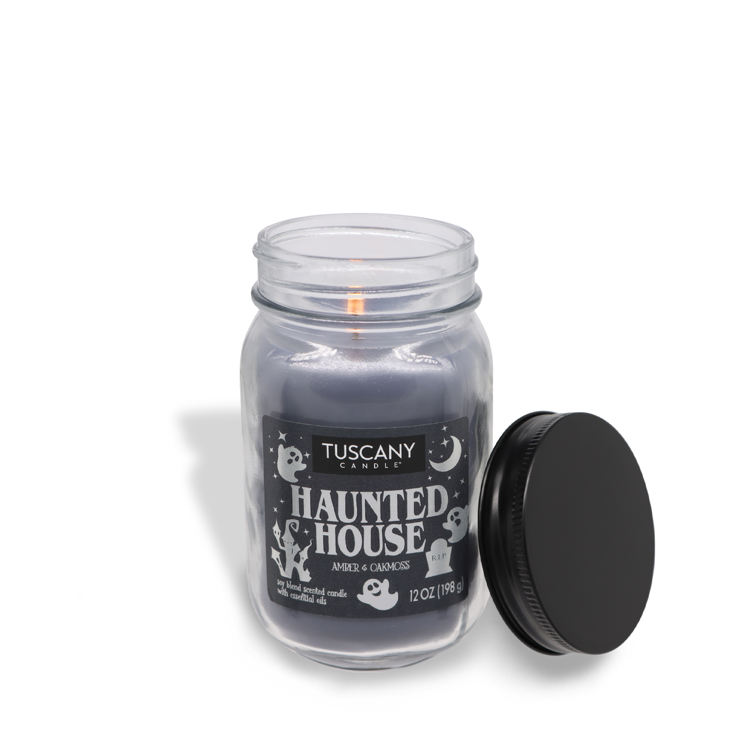 A lit Tuscany Candle® SEASONAL "Haunted House Long-Lasting Scented Jar Candle (12 oz)" label, featuring ghosts and bats, made from premium satin wax. The candle is in a glass jar, and the black lid is placed beside it. This treasure is part of their limited-run collection of scented jar candles.