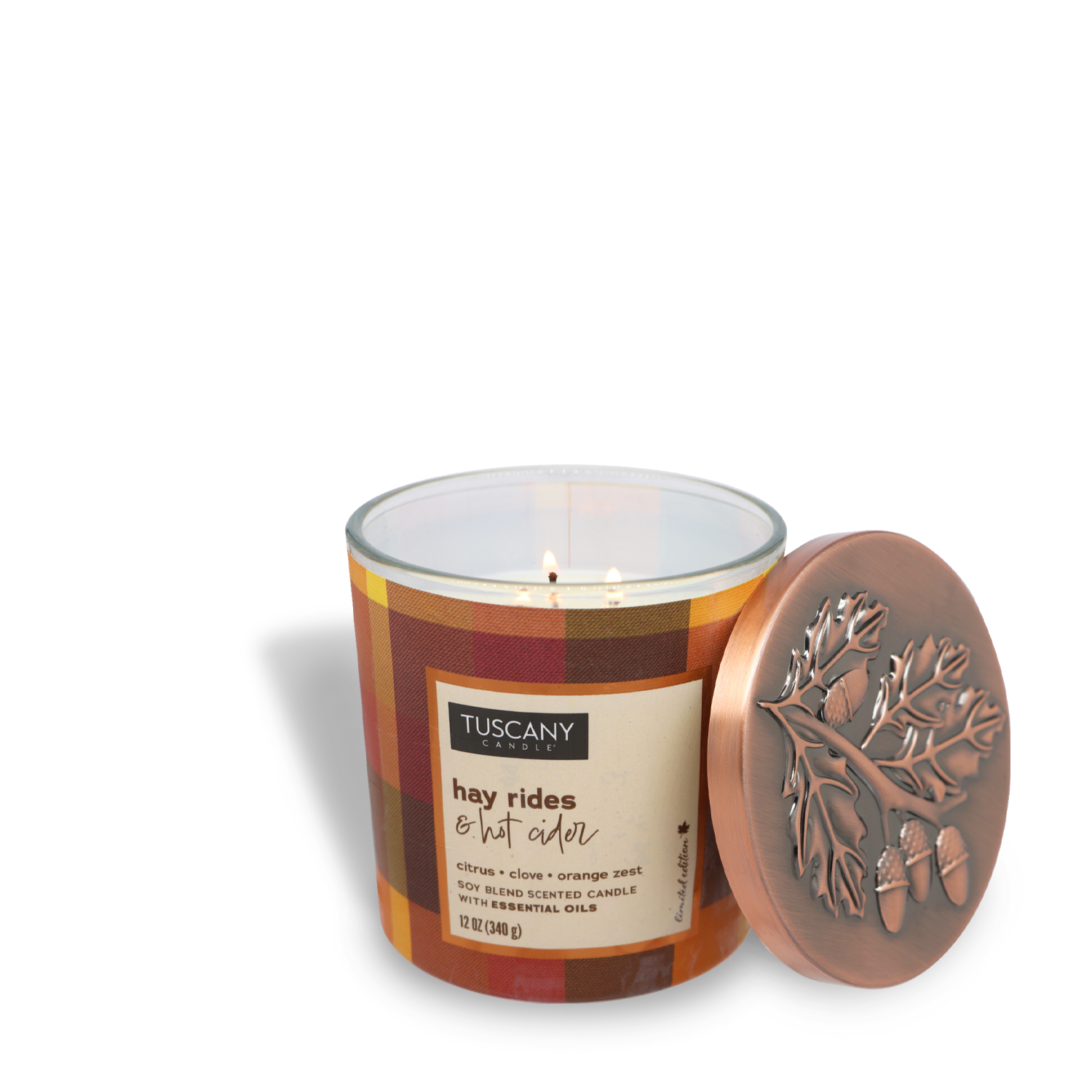 A lit Hay Rides & Hot Cider Long-Lasting Scented Jar Candle (12 oz) from the Autumn Flannels Collection by Tuscany Candle® SEASONAL, encased in a plaid-patterned jar with a label reading "Hay Rides & Hot Cider." The lid, placed next to the candle, features an embossed oak leaf and acorn design.