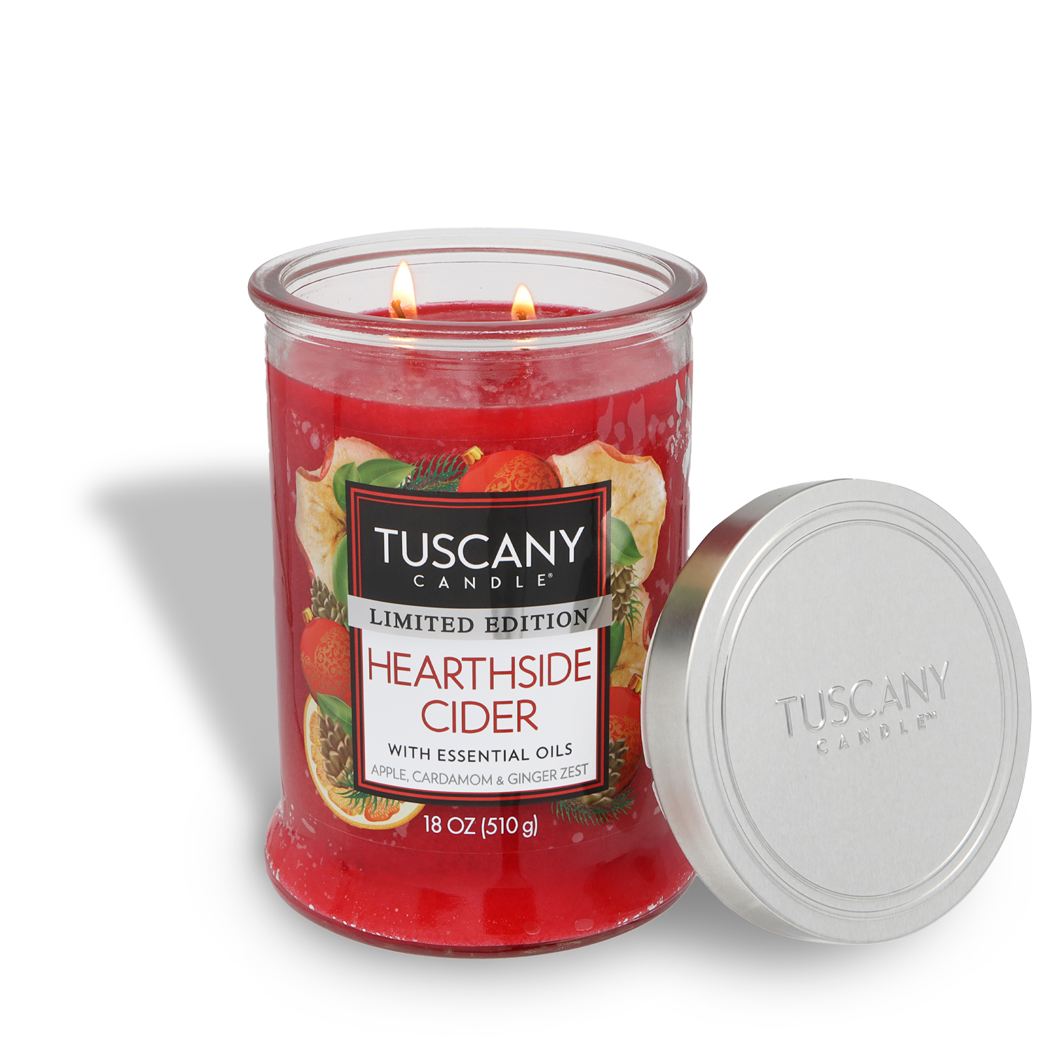 An 18 oz Tuscany Candle® SEASONAL “Hearthside Cider: Spiced Apple Cider Scented Holiday Candle” with a silver lid leans against it. The red candle has two lit wicks.