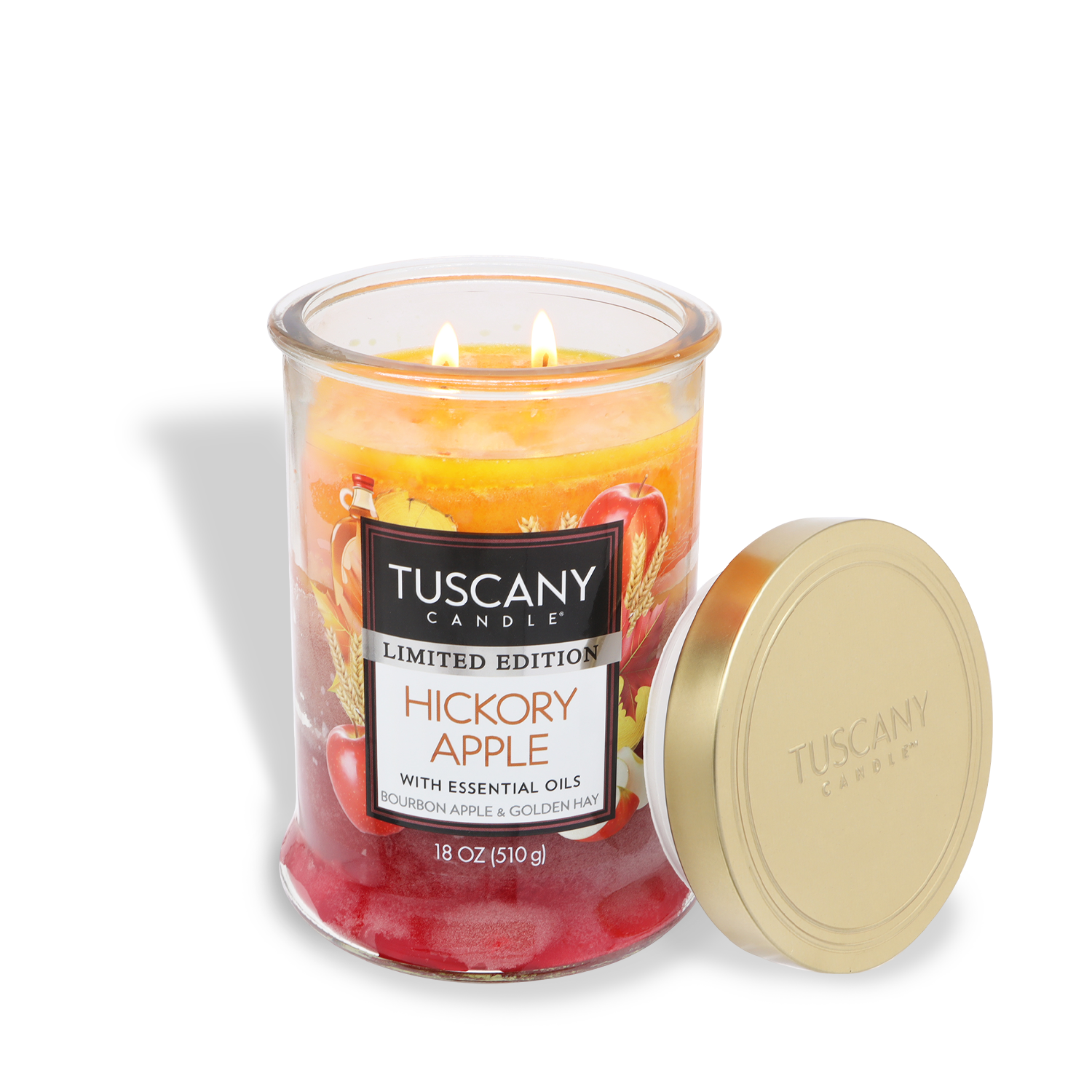 An 18 oz Tuscany Candle® SEASONAL in a glass jar labeled "Hickory Apple: Bourbon & Maple Syrup Scented Fall Candle" sits with two lit wicks and its gold lid placed beside it.