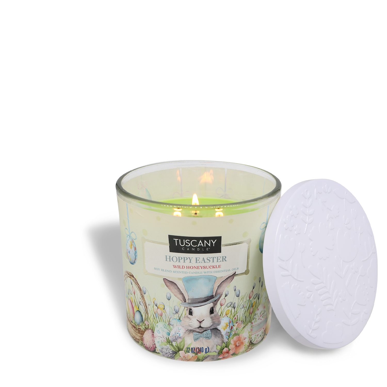 The Tuscany Candle® SEASONAL "Hoppy Easter" features a honeysuckle-scented candle in a glass jar with an Easter bunny and text design. Its lid, with embossed floral patterns, rests beside the 12 oz candle.