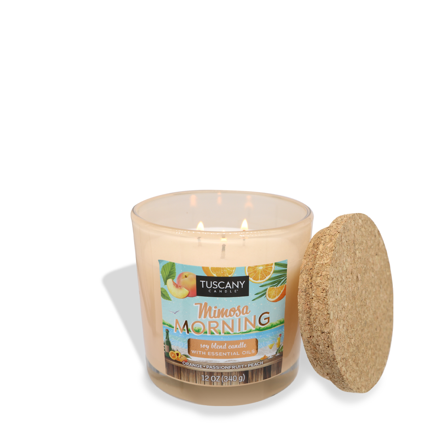 A glass jar candle labeled "Mimosa Morning (12 oz) – Sunset Beach Bar Collection" with essential oils by Tuscany Candle® SEASONAL, featuring citrus and peach imagery on the label. The candle is lit, its warm glow enhancing the vibrant design, while the cork lid is placed to the side.