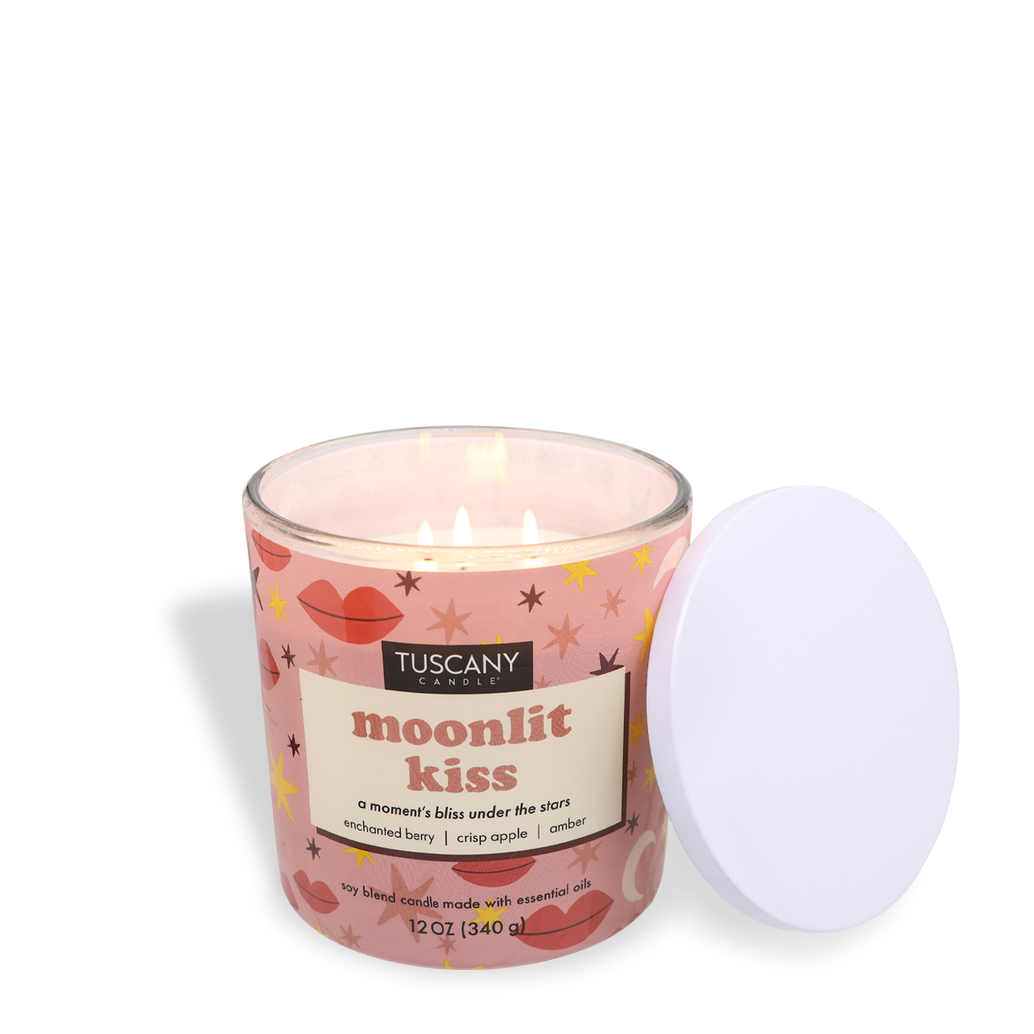 A lit Valentine's candle in a pink jar adorned with stars and lips rests beside its lid. Its label reads "Tuscany Candle® SEASONAL, Moonlit Kiss: Berry Scented Valentine’s Day Candle (12 oz), blackened berry, crisp apple, amber," making for a romantic fragrance.